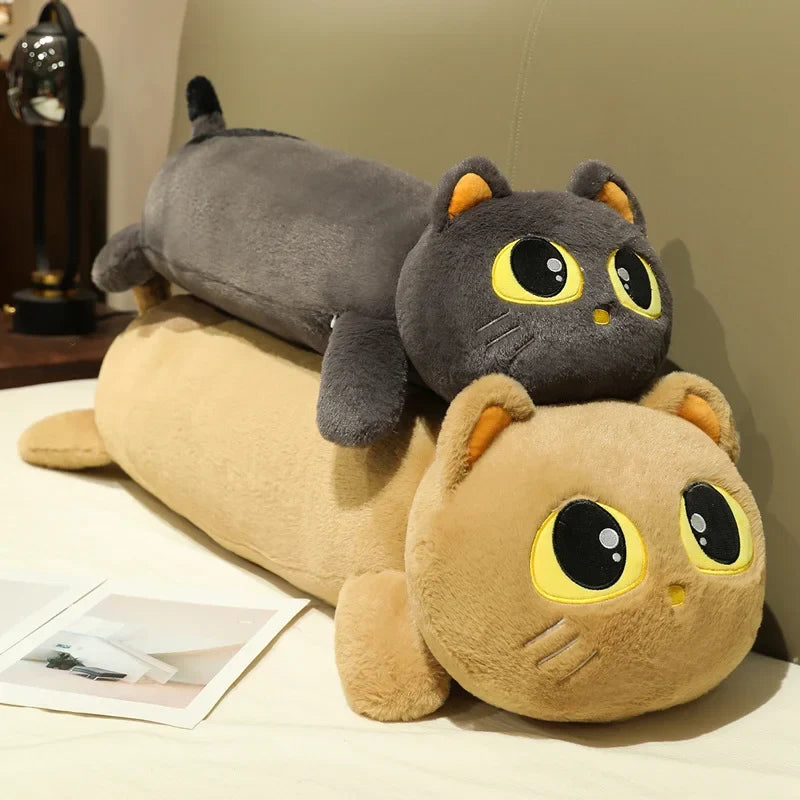Two big-eyed gray and beige cat plush pillows cuddled together on a bed