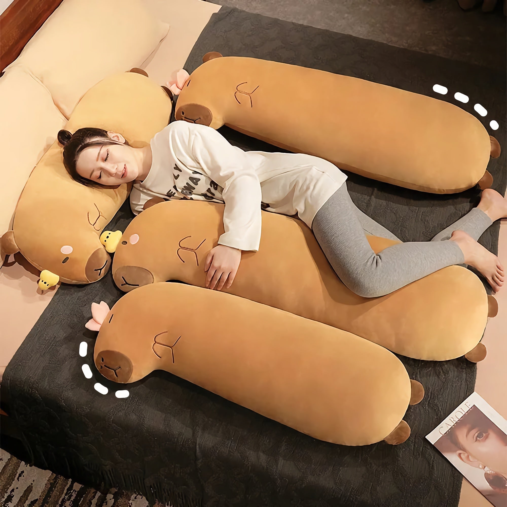 Person lying on a bed hugging a large elongated capybara body-pillow plush