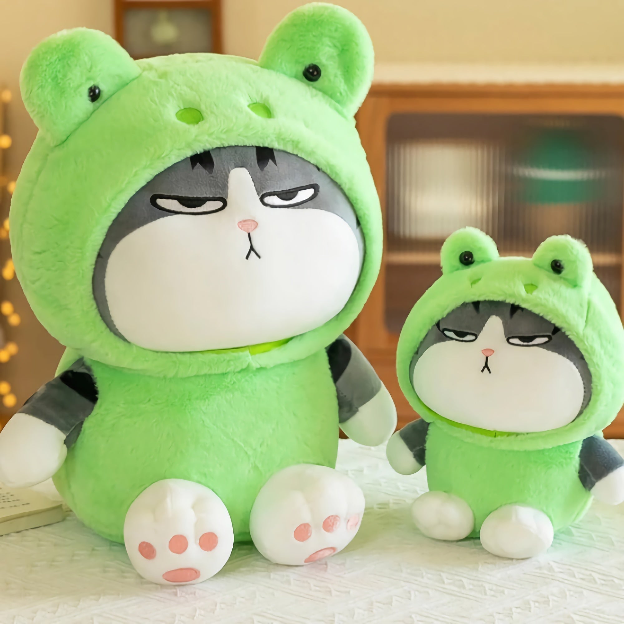 Two stylized kawaii cat plushies wearing frog hoodies, one large and one small, with expressive faces