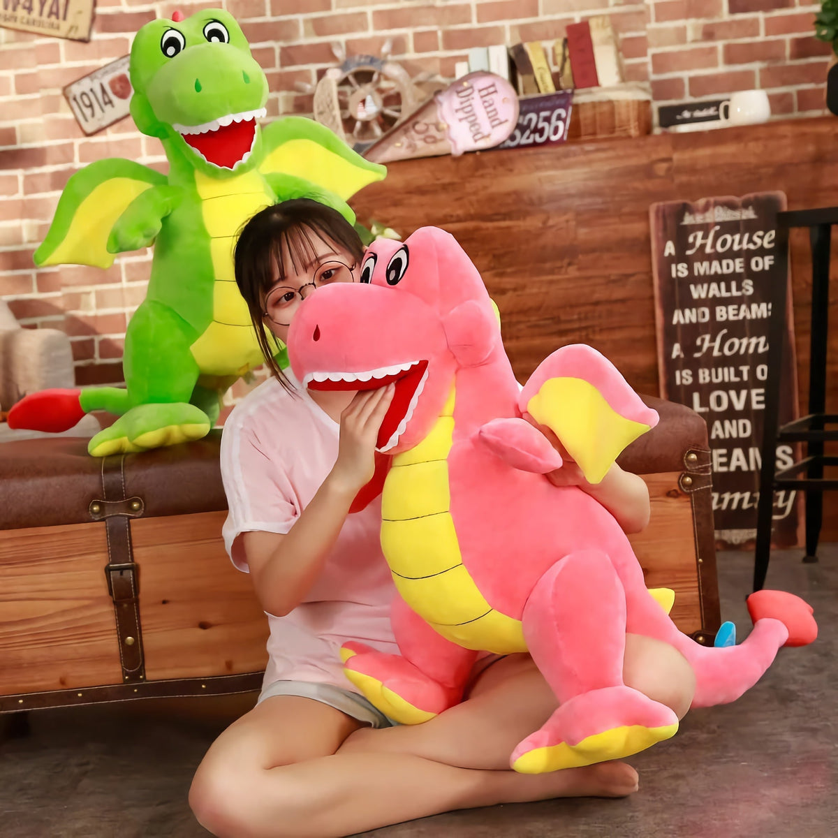 Young girl sitting on the floor hugging a large pink dinosaur plush toy with a green dinosaur plush beside her