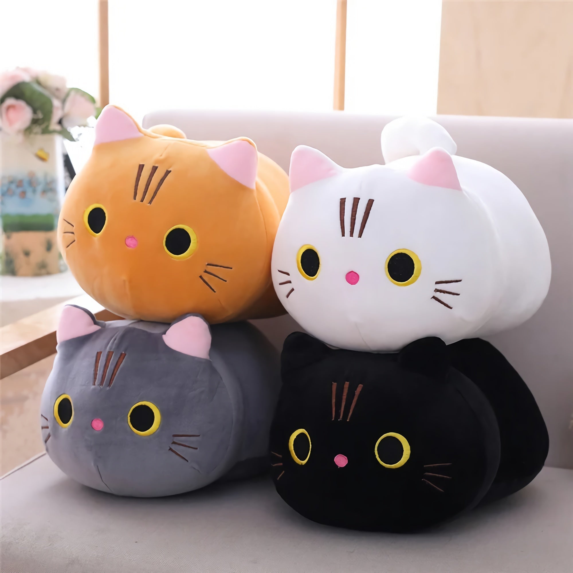 Round plush cat pillows in orange, white, gray, and black, stacked on a couch