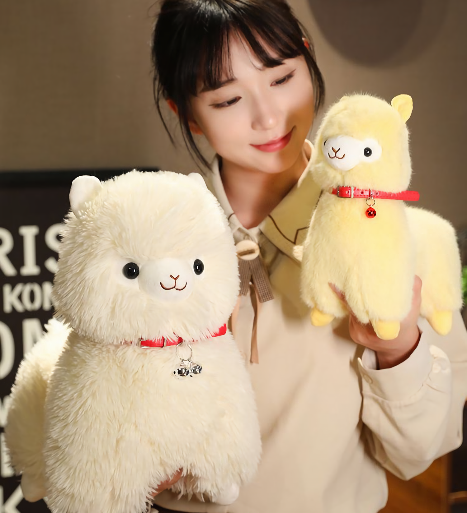 Girl holding a yellow alpaca plush next to a white alpaca plush with a red bell collar