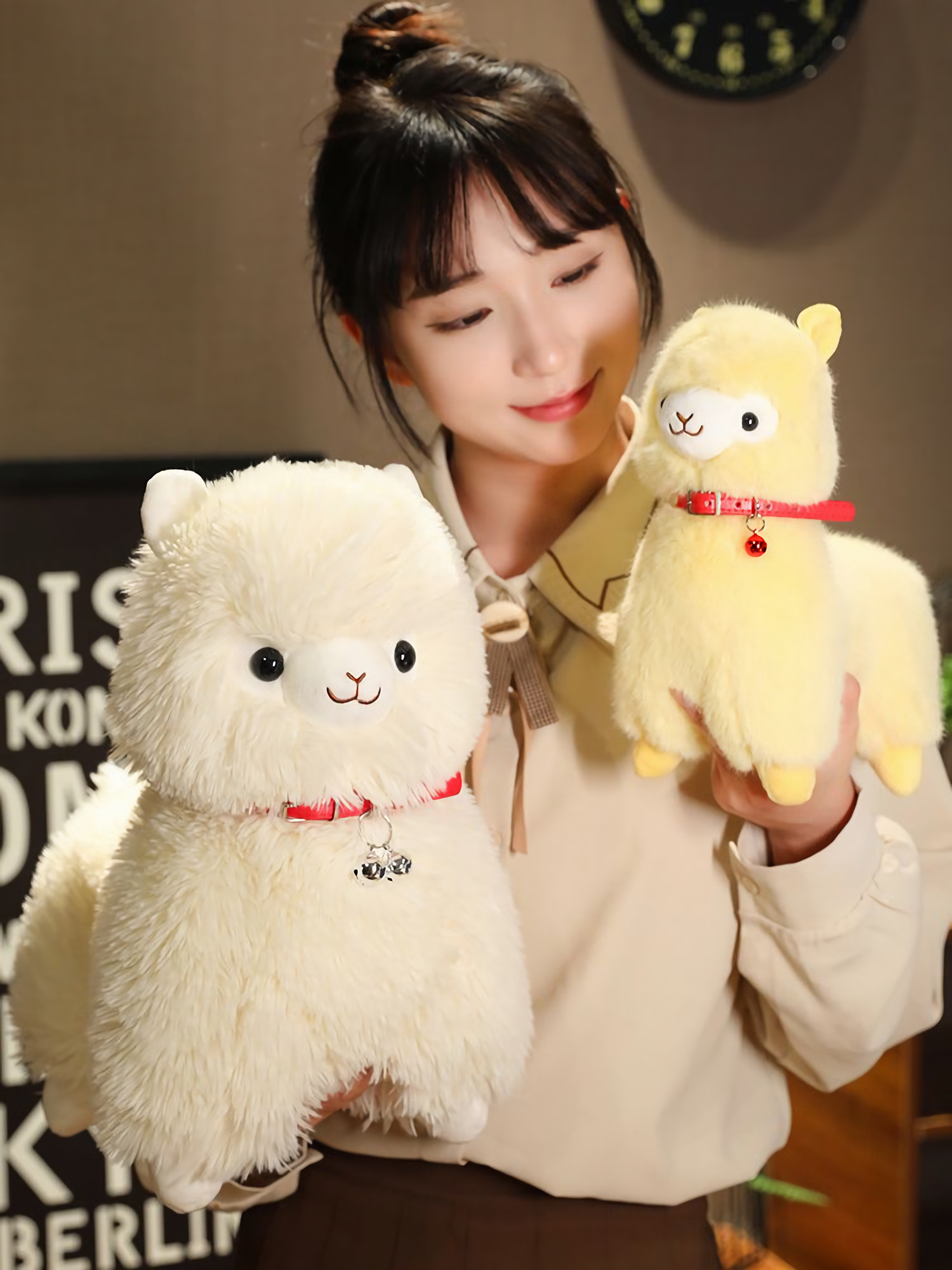 Girl holding a yellow alpaca plush next to a white alpaca plush with a red bell collar