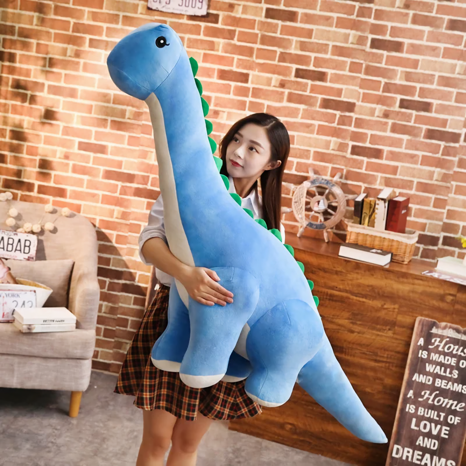 Woman hugging a large blue Brachiosaurus plush with cream belly and green spikes, standing in a cozy room.
