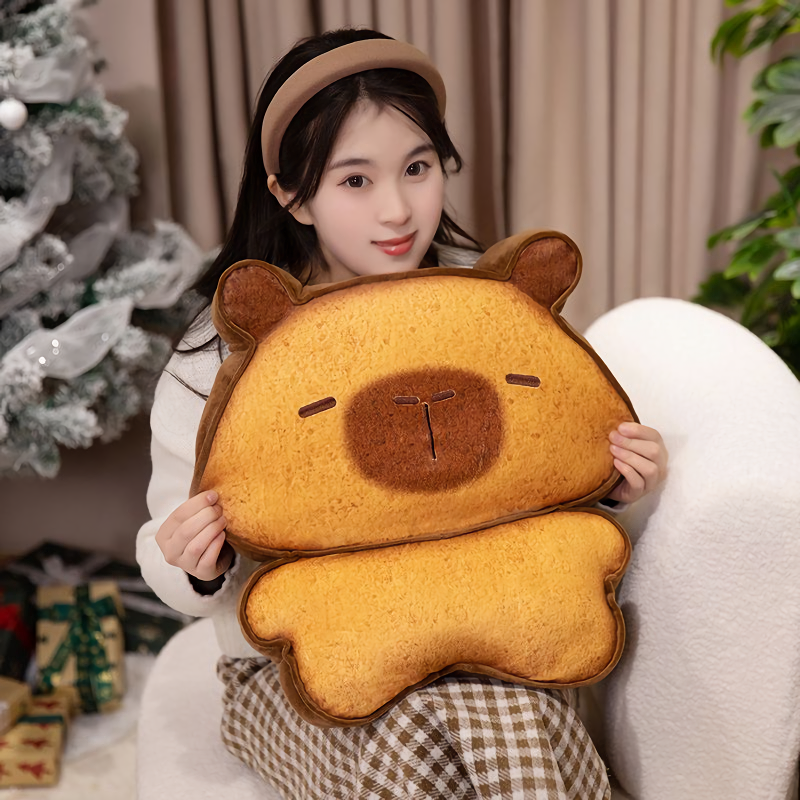 Woman holding a bread capybara plush in front of a Christmas tree