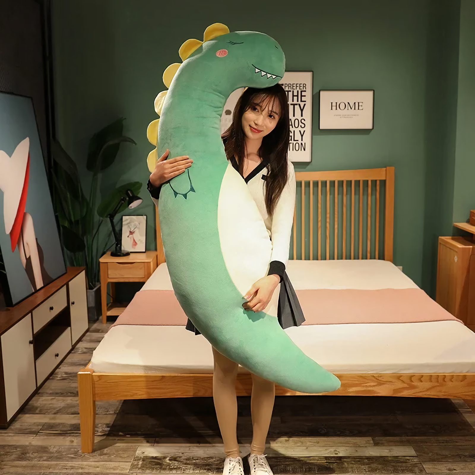 Woman standing in a bedroom holding a tall curved green dinosaur plush body pillow