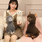 Woman sitting on a bed with gray, white and brown fluffy alpaca plushies