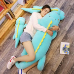 Woman lying on a wood floor hugging a long blue dinosaur plush body pillow beside a smaller one