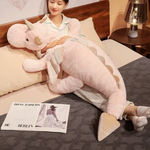 A woman on a bed hugs a pink and white dragon plush body pillow with wings and horns.