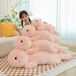 Woman sits beside stacked pink dinosaur plush pillows in four sizes on a checkered rug.