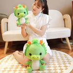 Woman holding smaller green dragon plush with larger one on carpet.
