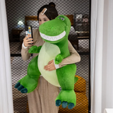 Woman holding a big friendly green T-Rex dinosaur plush with a toothy smile, taking a selfie.