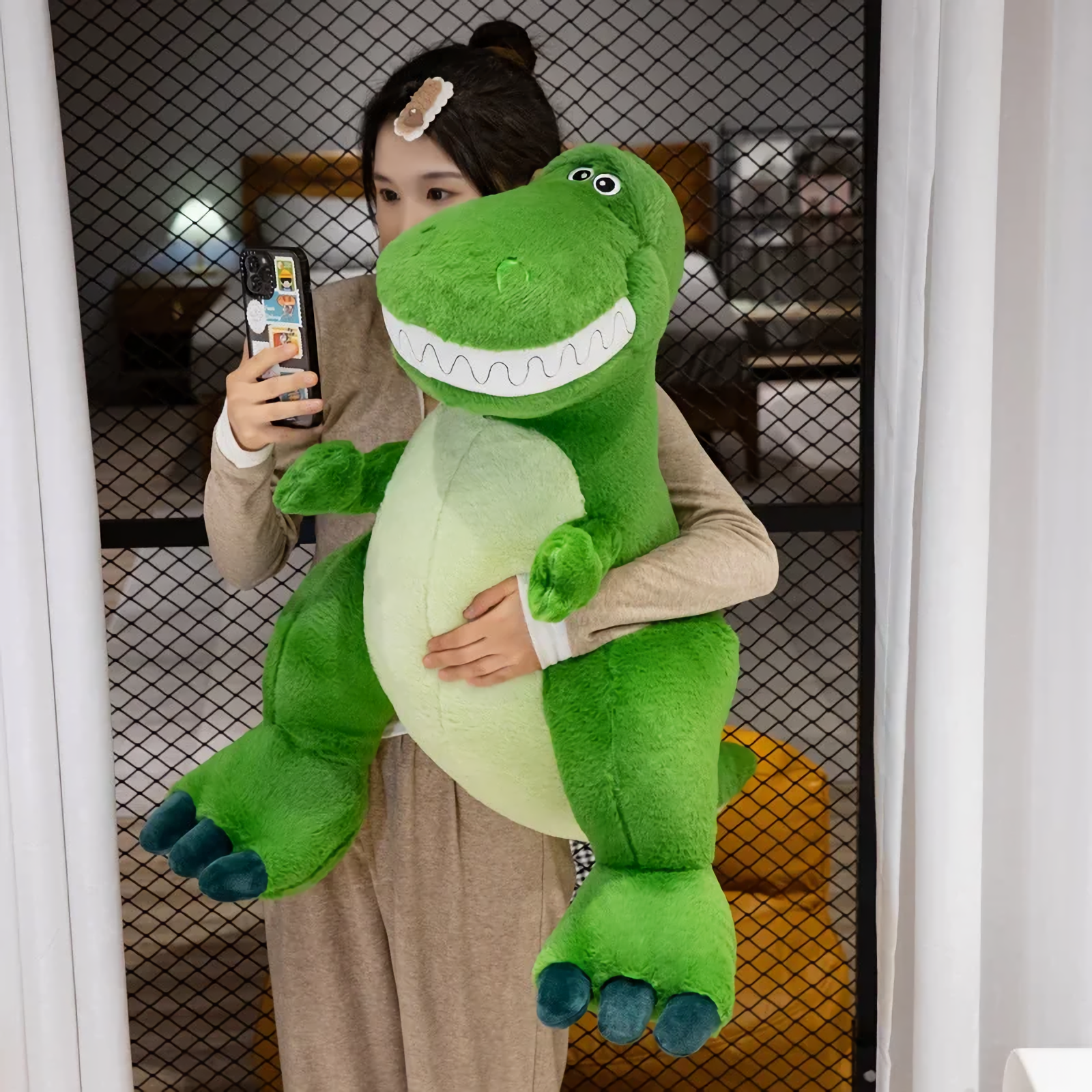 Woman holding a big friendly green T-Rex dinosaur plush with a toothy smile, taking a selfie.