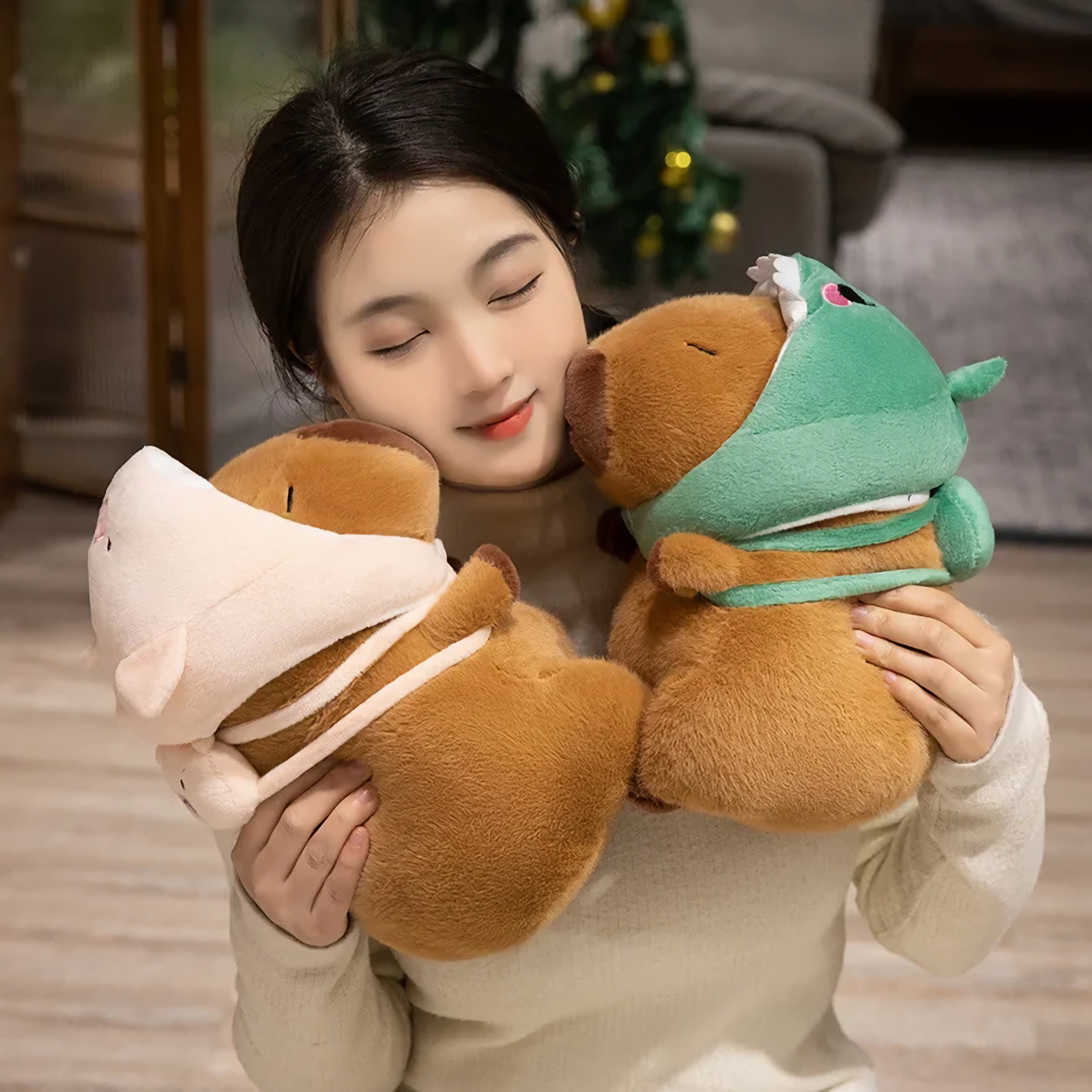 Woman holding two capybara plushies wearing pig and dinosaur hoods