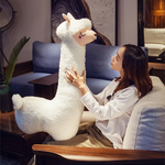 Woman sitting on a sofa touching the face of a tall white alpaca plush body pillow