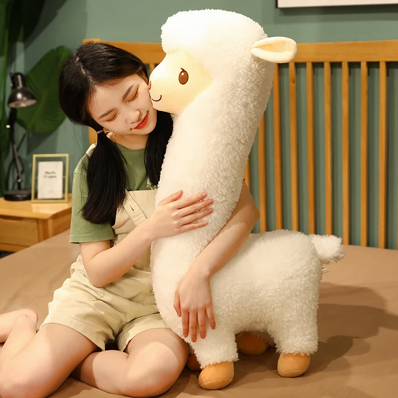 Woman sitting on a bed hugging a tall white alpaca plush with a long neck