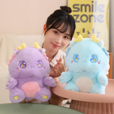 A woman with a purple and a blue baby dragon plush on a table, showing off their golden horns and sparkly eyes.