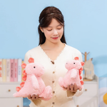 Woman holding two pink dinosaur plush toys in front of a blue wall