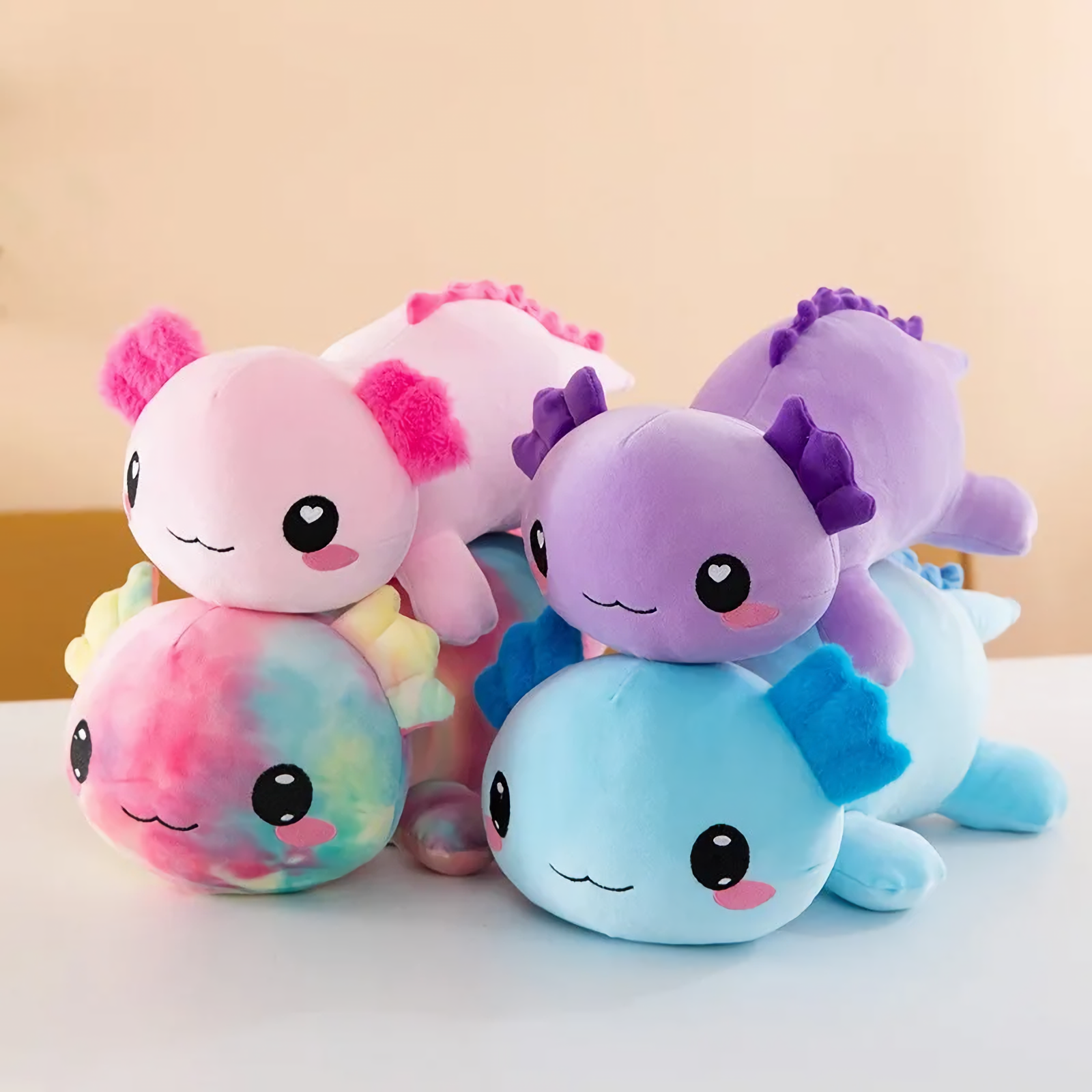 Rainbow, pink, purple and blue axolotl plush pillows stacked together on a white table