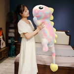 Woman in a white dress holding a tall pink rainbow dinosaur plush body pillow upright