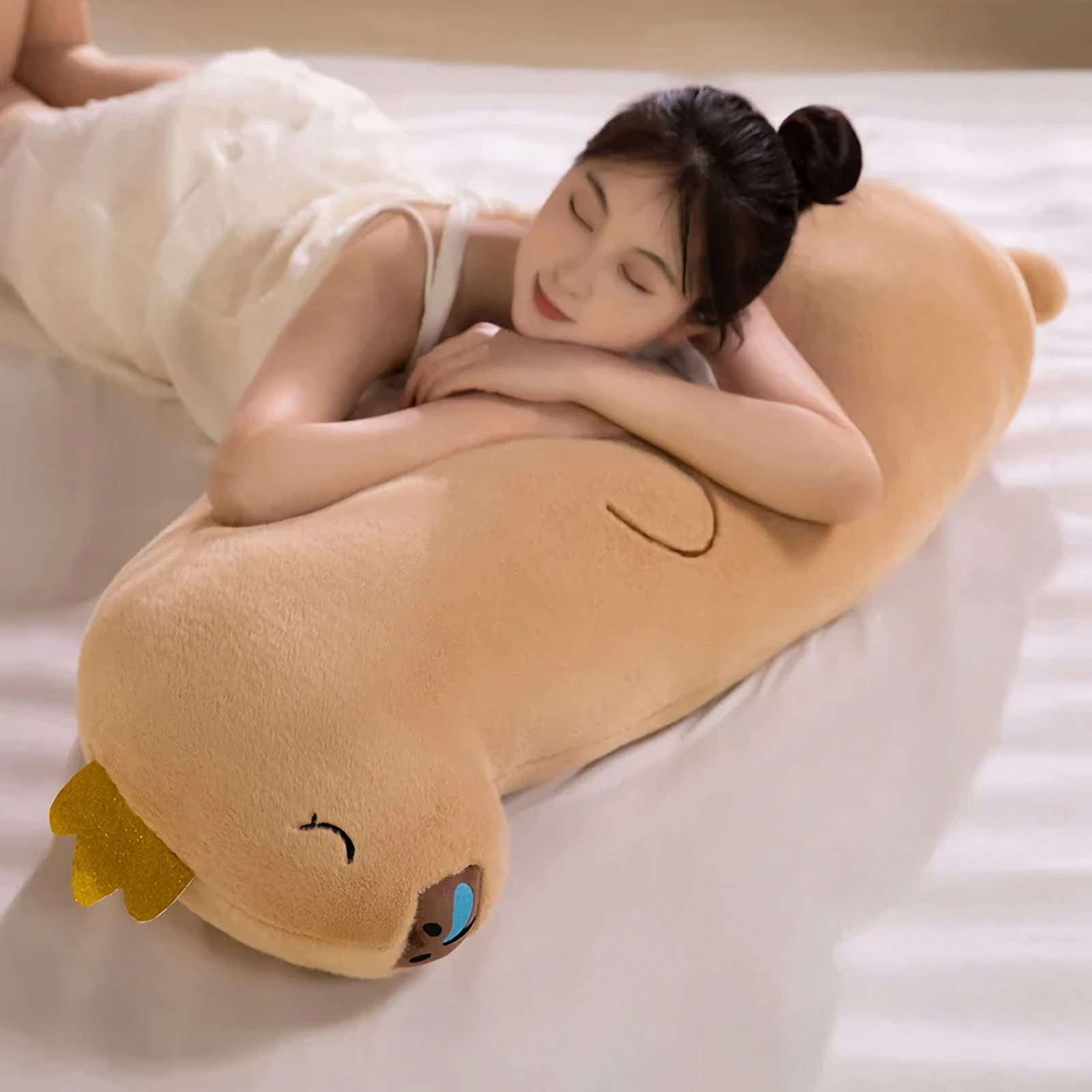 Woman lying on a bed hugging a long tan capybara body pillow with a gold crown
