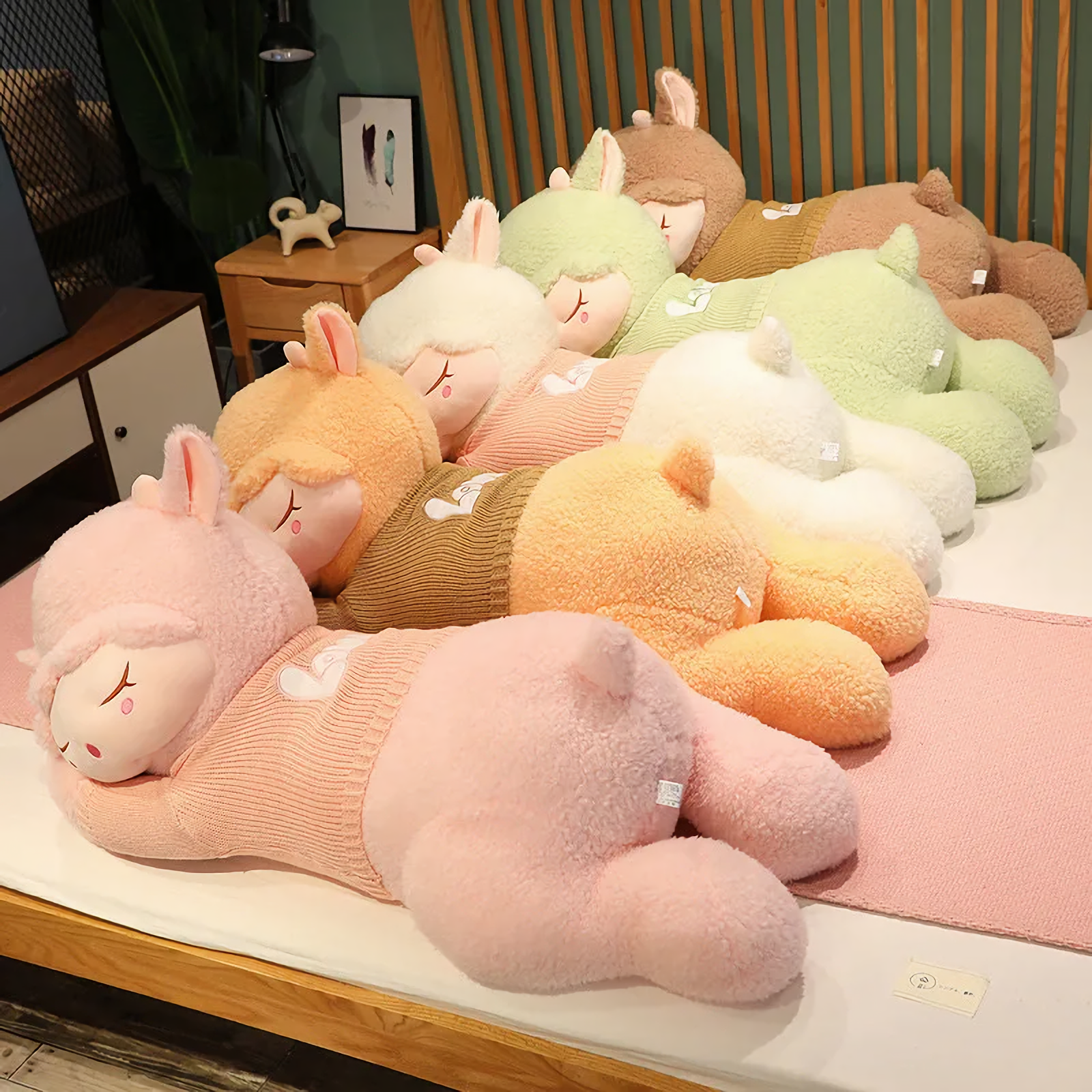 Five sleeping sheep plush pillows in pink, orange, white, green and brown lying in a row on a bed