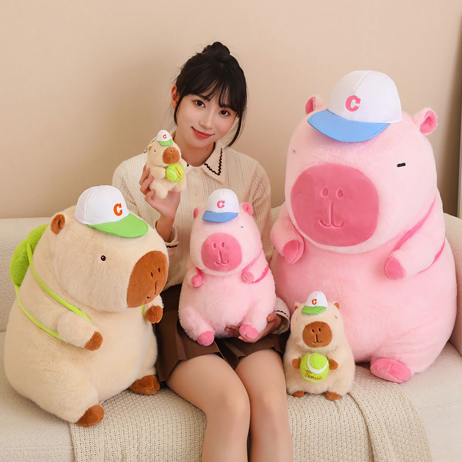 Woman on a sofa holding sporty pink and brown capybara plushies with white caps