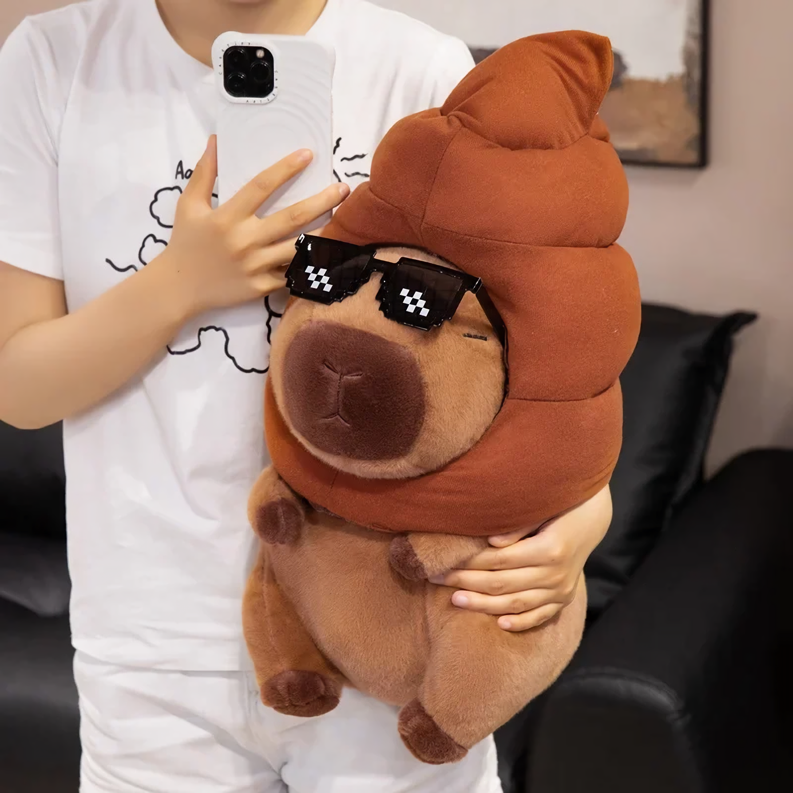 Person holding a capybara plush with a brown swirl hat and pixel sunglasses