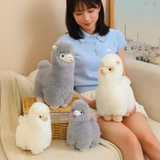 Woman sitting on a sofa with gray and white alpaca plushies in two sizes around her