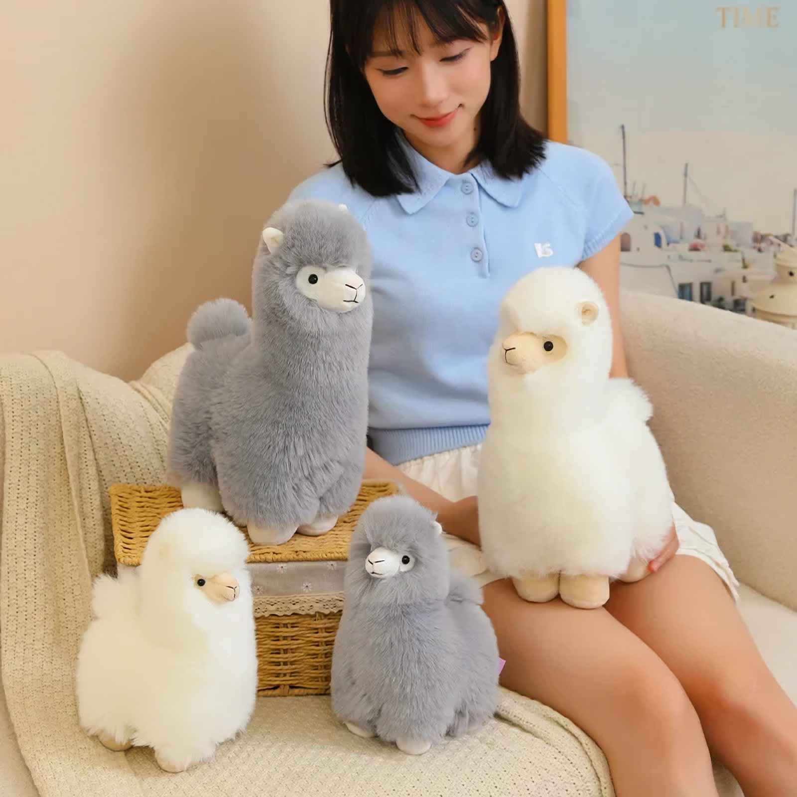 Woman sitting on a sofa with gray and white alpaca plushies in two sizes around her