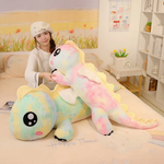 Woman in a white knit hat with a rainbow dragon plush and a green rainbow dragon plush on a bed