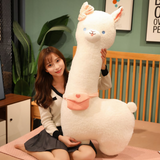 Woman sitting on a bed holding a large white alpaca plush with a pink bow and bag