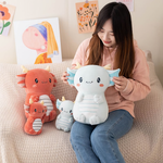 Girl sitting on a sofa holding a light blue axolotl dragon plush next to two burgundy ones