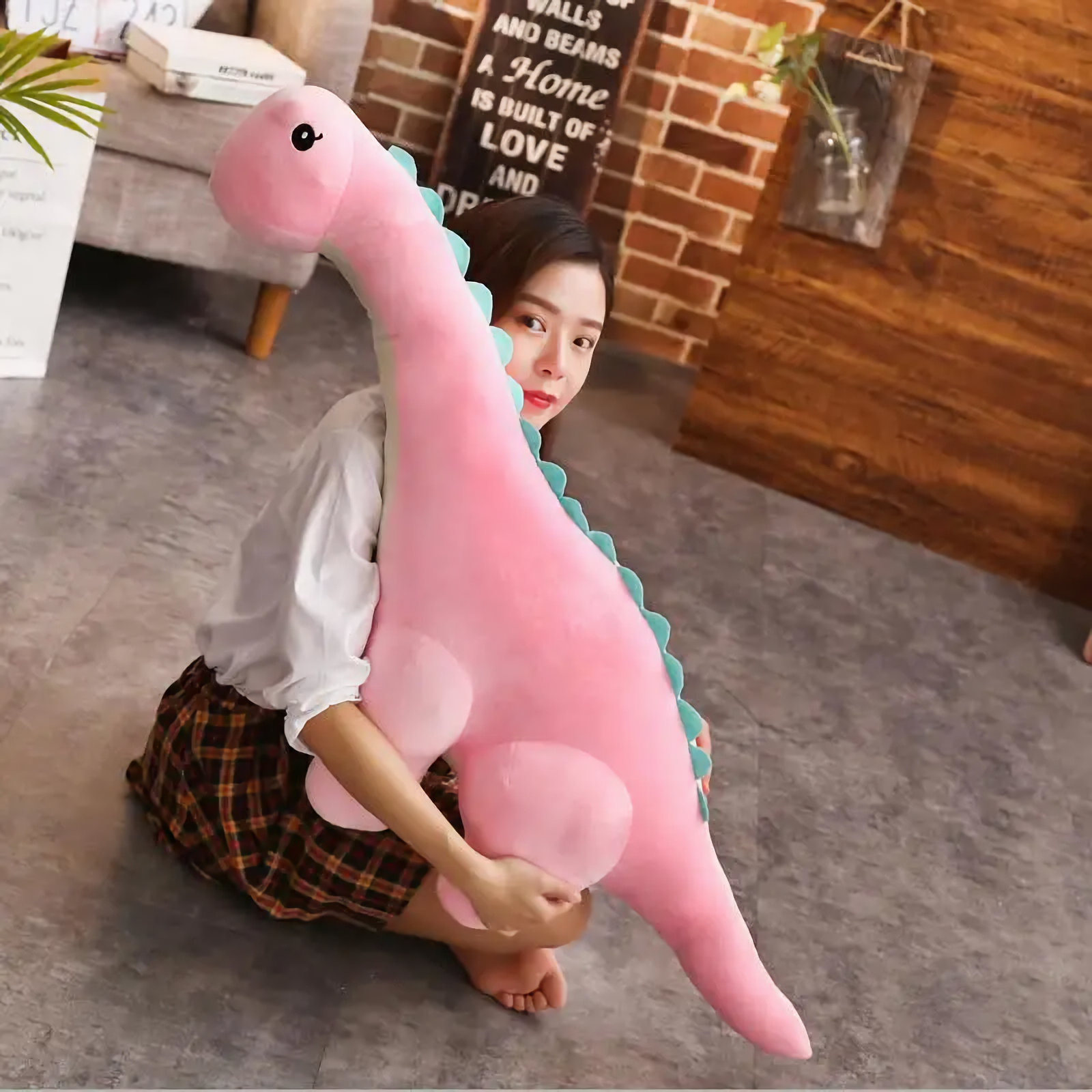 A woman sitting on the floor hugging a pink Brachiosaurus plush.