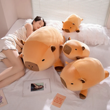 Woman lying on a bed beside three chubby capybara plush pillows of different sizes