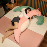 Woman lying on a bed with a curved pink unicorn plush pillow and a green dinosaur plush pillow