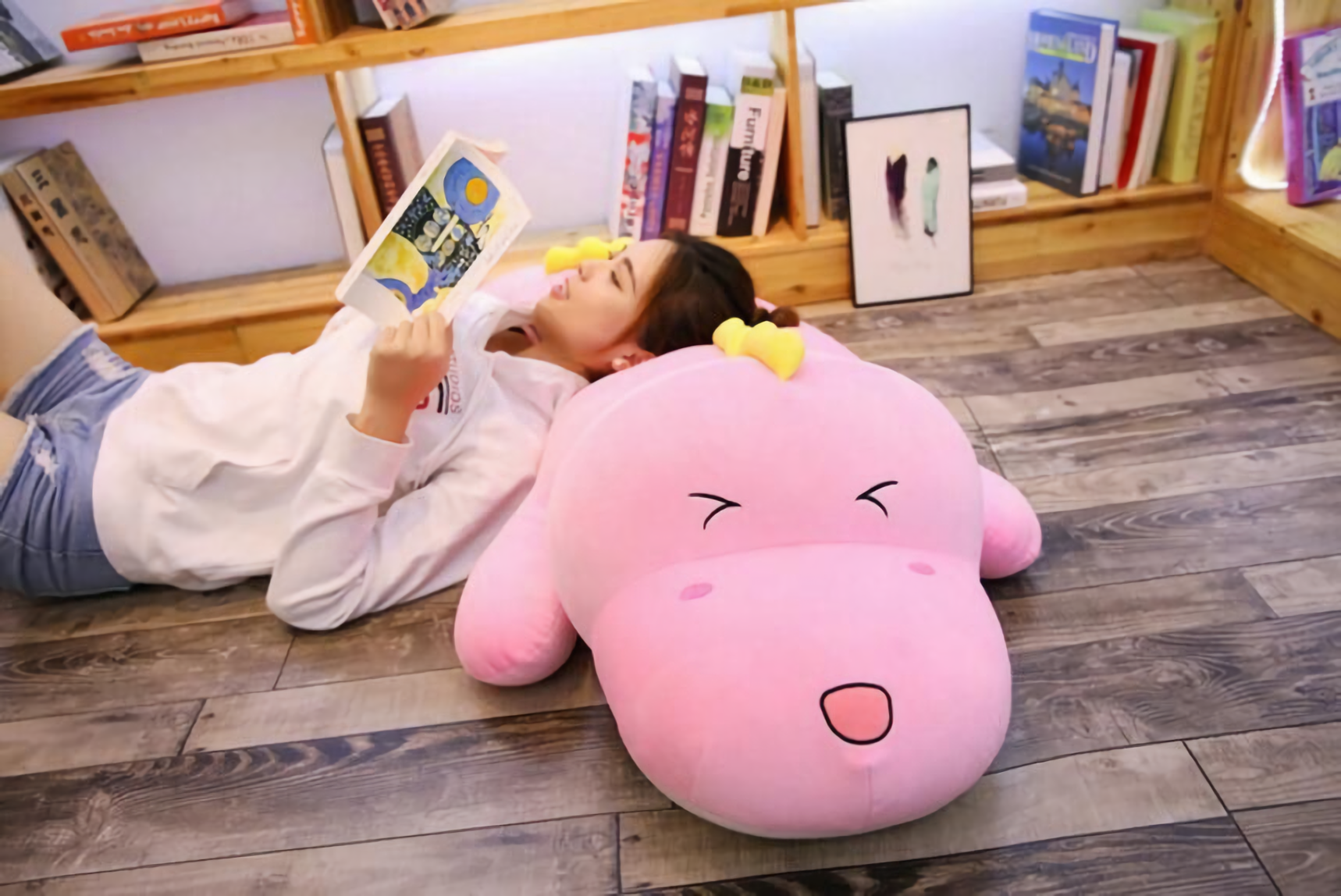 Girl lying on the floor reading with her head on a pink dinosaur plush pillow