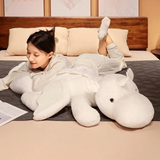 Woman lying on bed hugging a white dragon plush body pillow with small wings and horns.