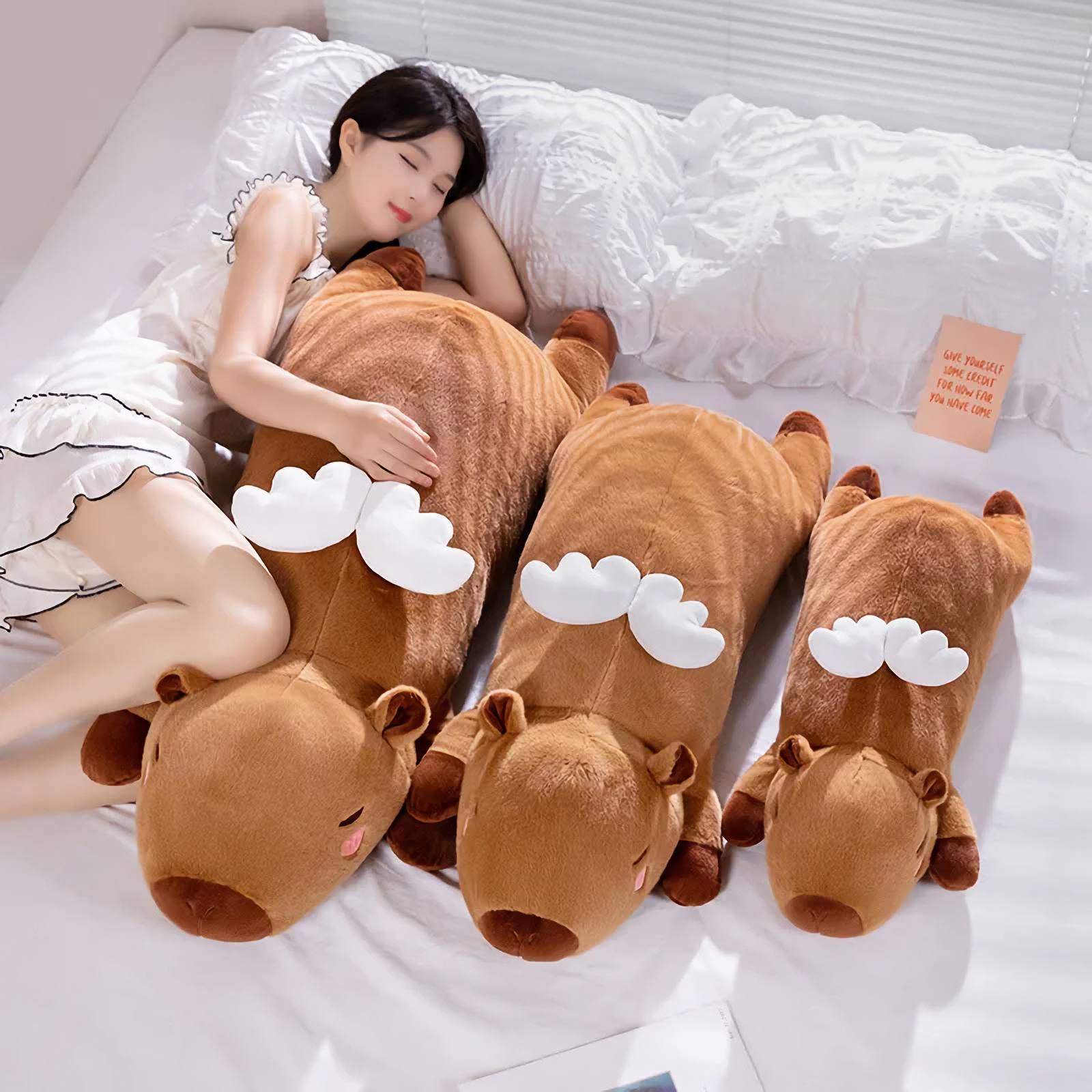 Woman sleeping on a bed with three lying brown capybara plush pillows with white wings