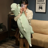 Woman holding mint green and white dragon plush body pillow, taking a photo with a smartphone.