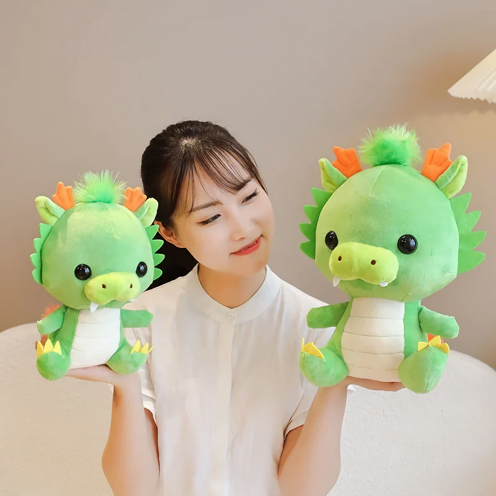 Woman holding two green dragon plush toys with orange horns.