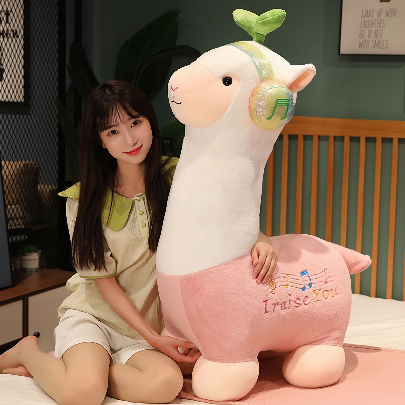 Woman sitting on a bed beside a large pink alpaca plush with music headphones