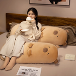 Woman drinking tea on a bed beside two tan capybara bolster pillows