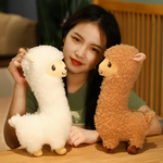 Woman smiling with a white alpaca plush and a brown alpaca plush on a bed