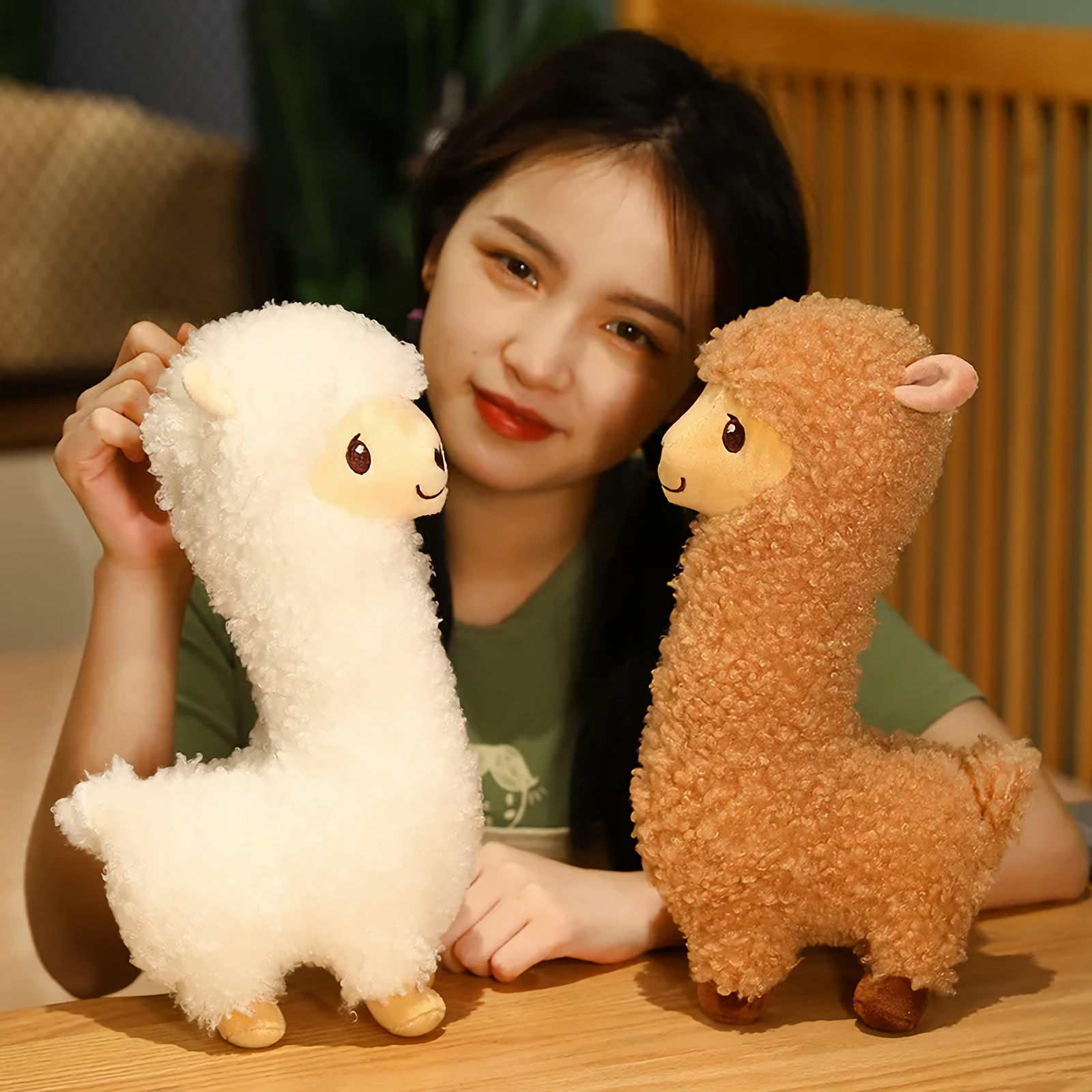 Woman smiling with a white alpaca plush and a brown alpaca plush on a bed