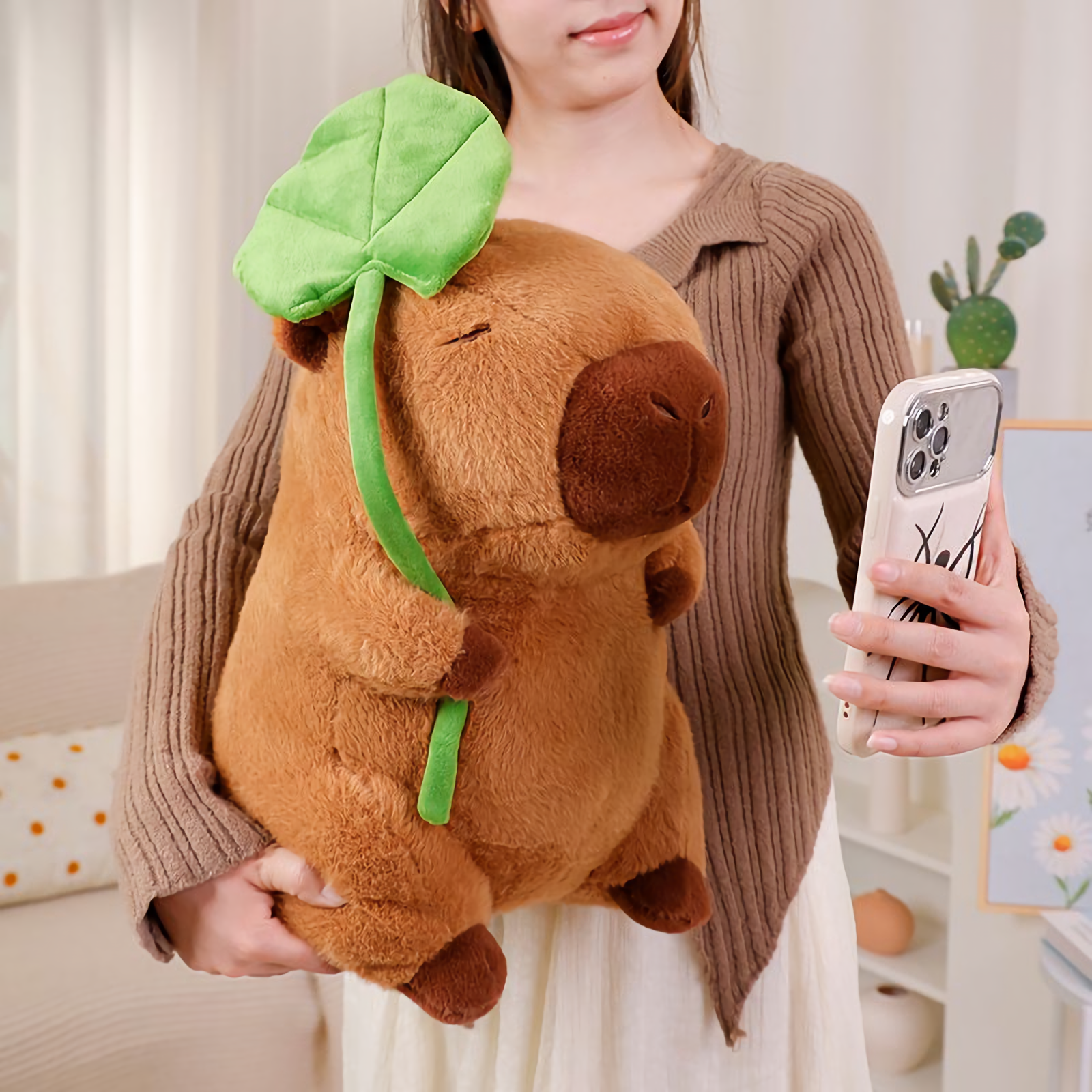 Woman holding a lotus leaf capybara plush and taking a phone photo