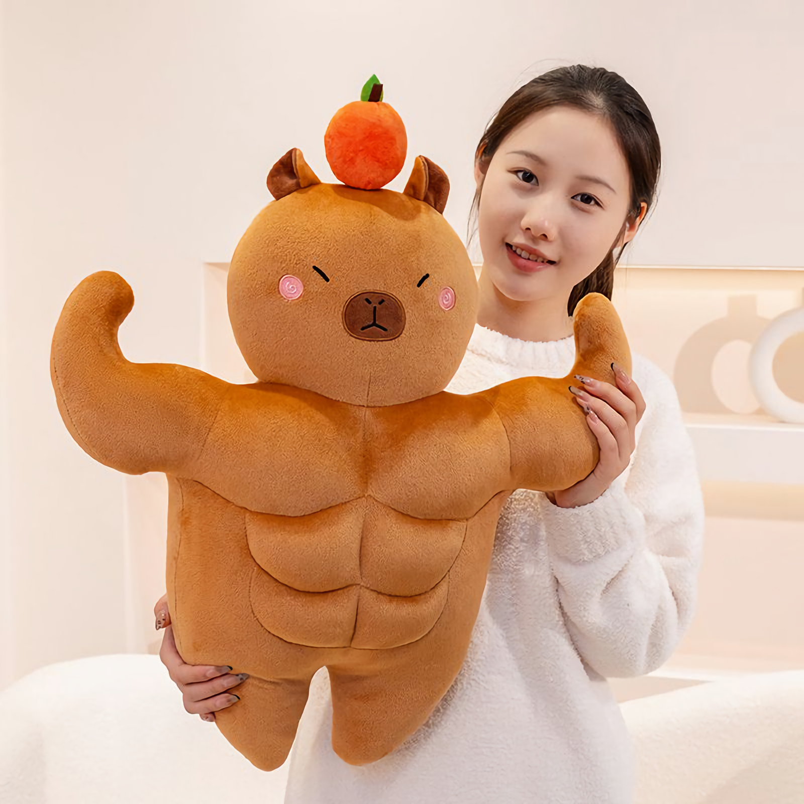Woman holding a muscle capybara plush with big arms and an orange on top
