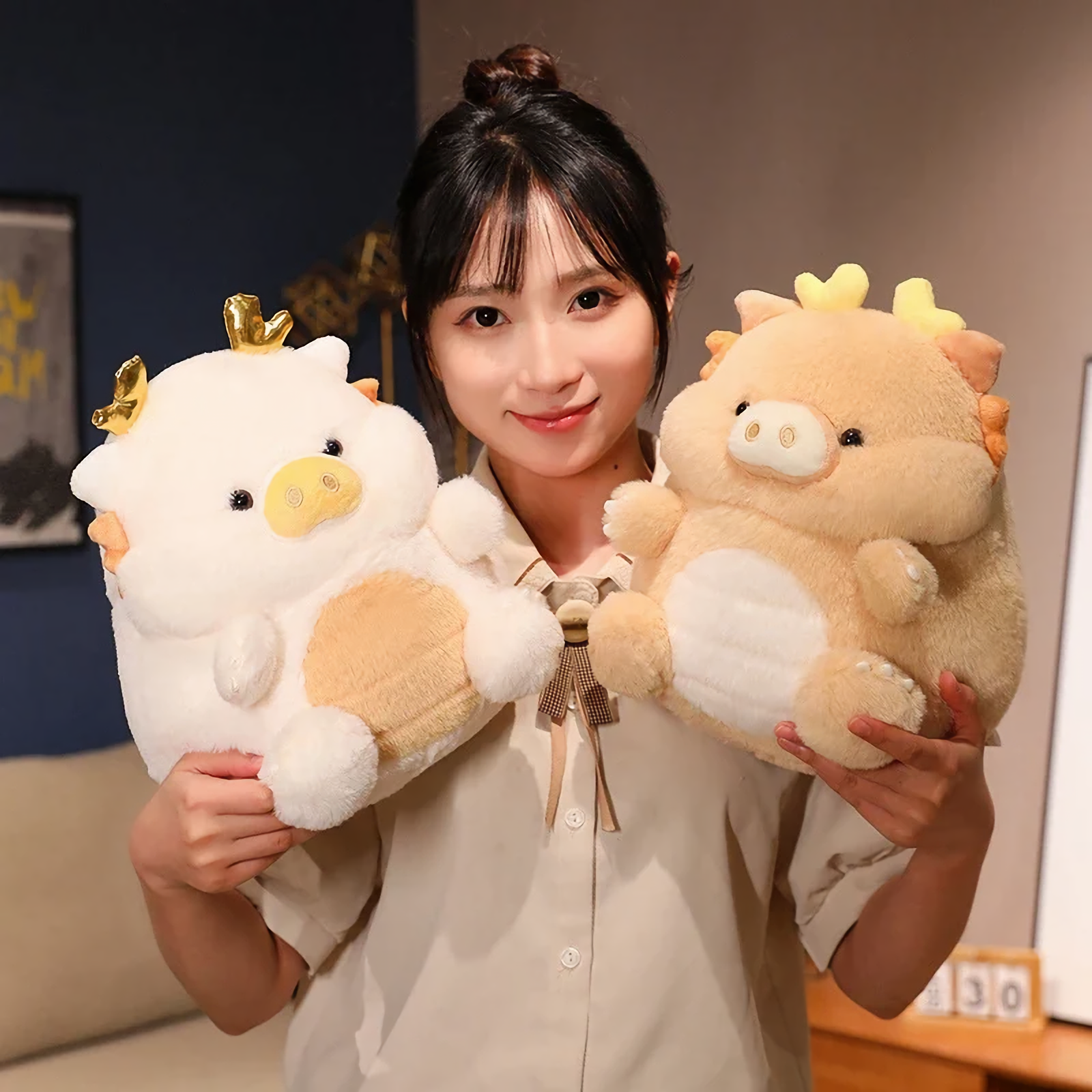Woman holding white and peach pig-dragon plush cushions, smiling indoors.