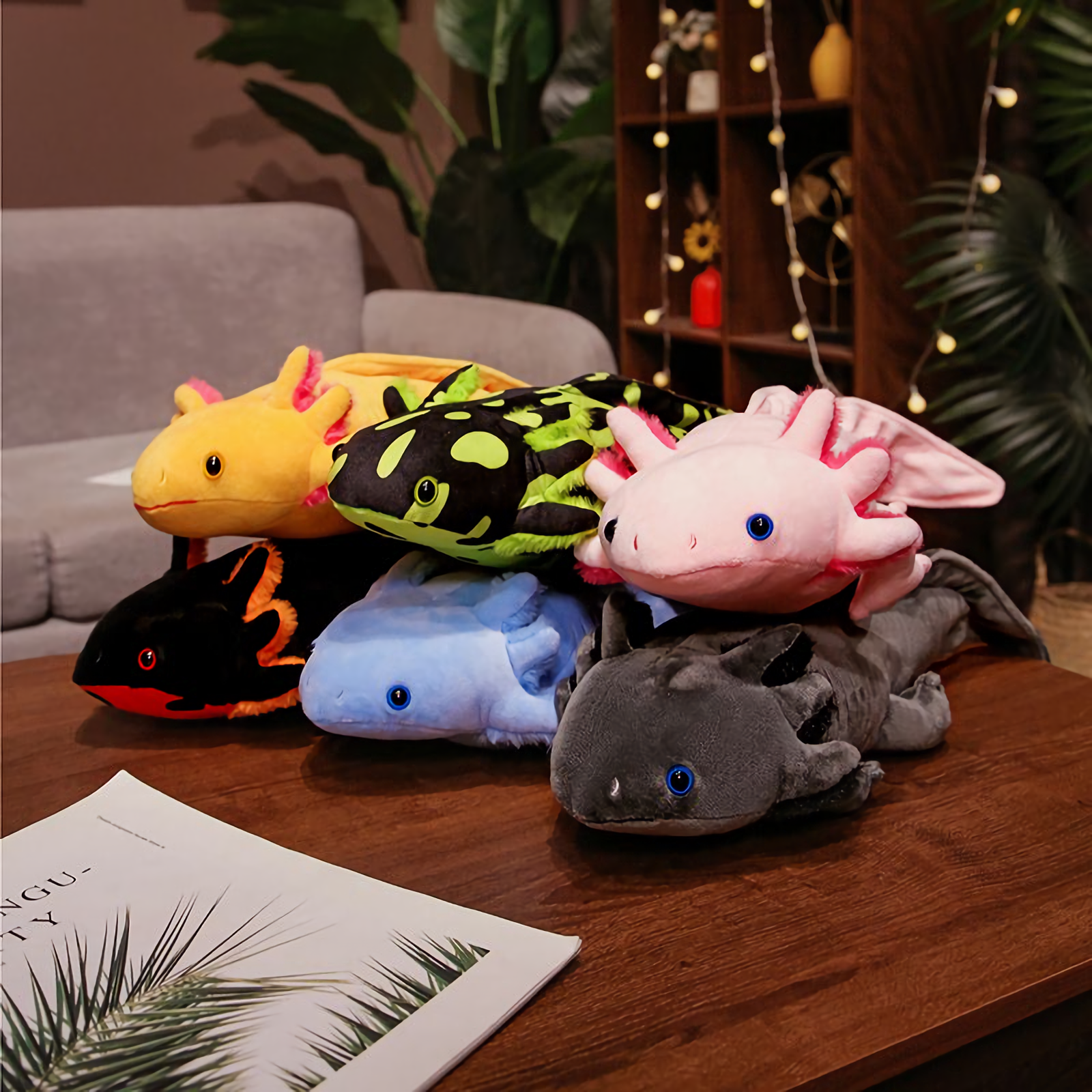 Pile of colorful axolotl plushies in yellow, spotted green, pink, blue, black and gray on a wooden table