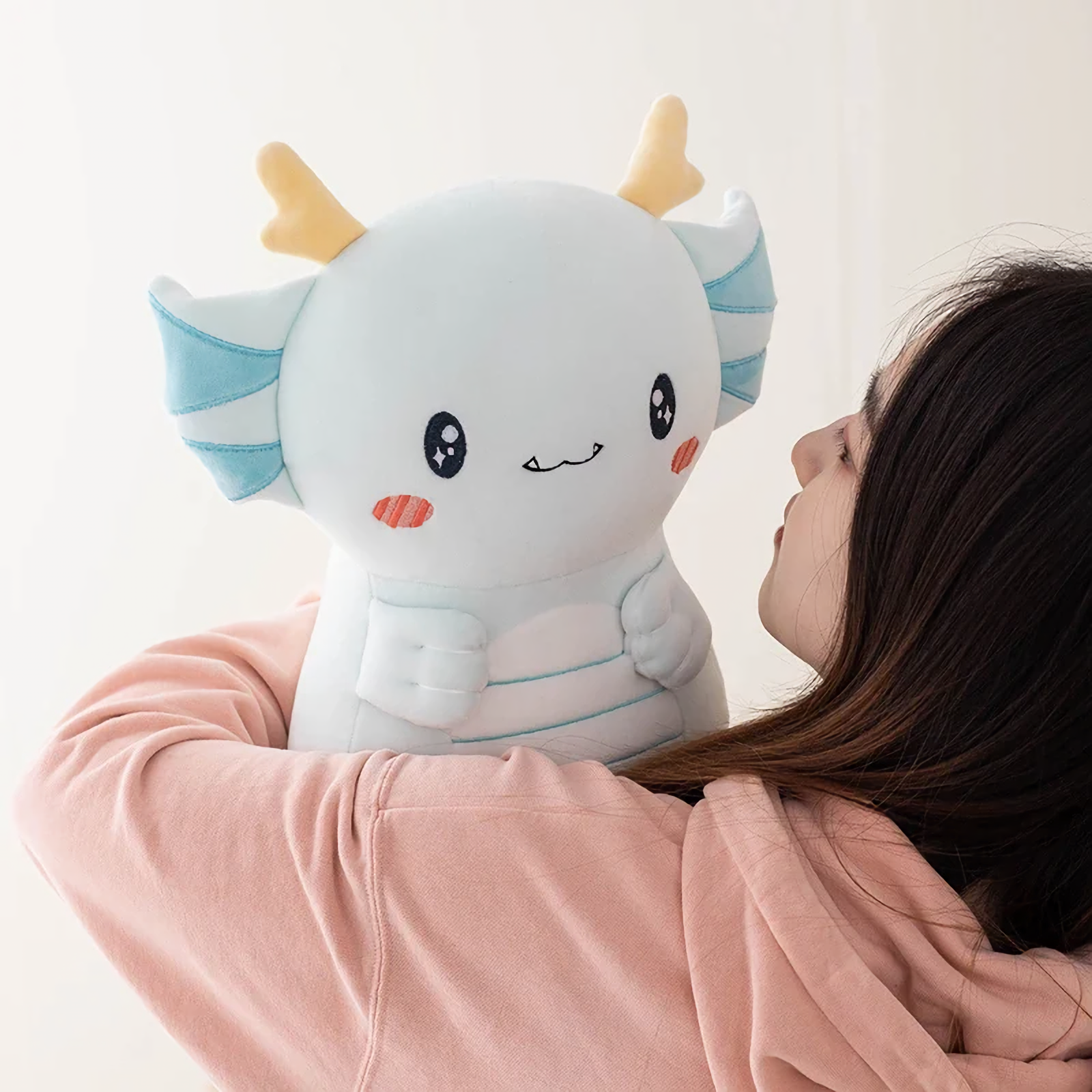 Girl looking at a light blue axolotl dragon plush on her shoulder
